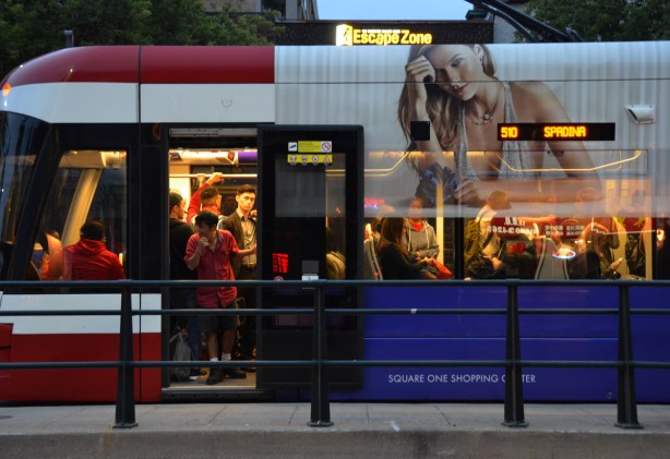 front end of a Spadina streetcar, evening, door ope as people getting on, ad on the outside with a picture of a woman, 