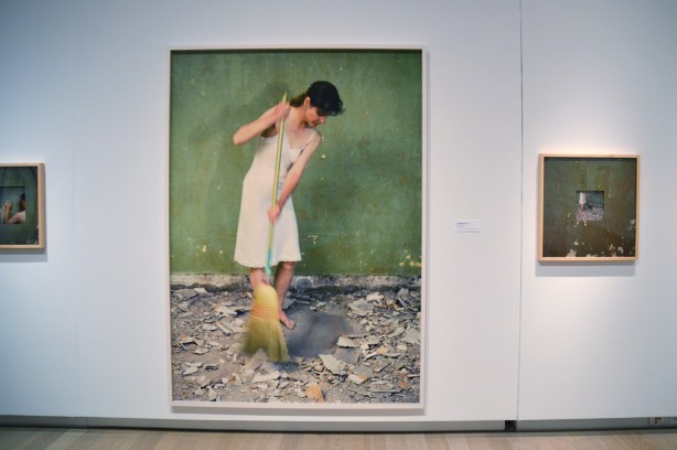  large photo in a gallery of a women dressed just in a long slip, sweeping up debris from the floor. Debris is bits and chunks of plaster that have been removed from the wall 