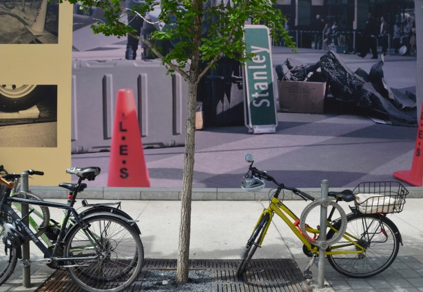 bikes parked in front of a large photo mounted on the side of the TIFF lightbox building, showing an orange movie shoot cone and a fake city street sign. 