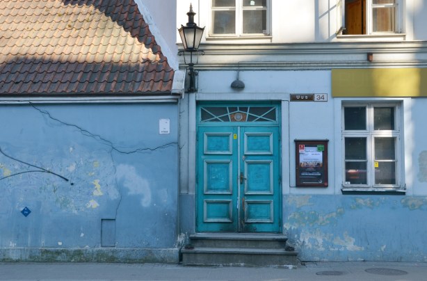 turquoise wooden double door with two steps up to it, on a house painted blue (lower part) and white (upper part). 