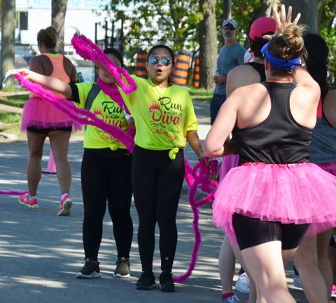 two volunteers in bright yellow t-shirts hand out pink boas to race particpants as they come close to the finish line
