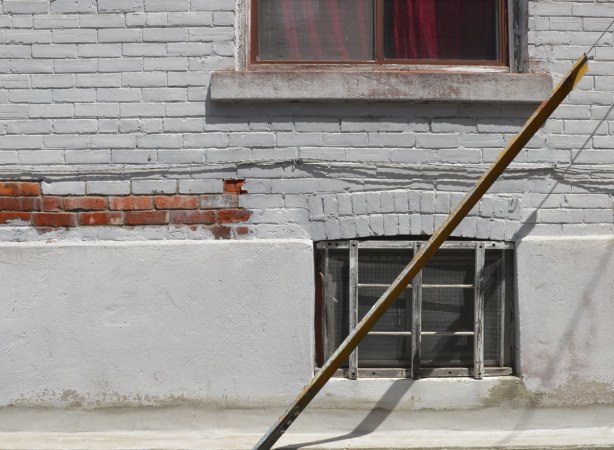 window with deep red curtain, grey painted brick wall, lower basement window