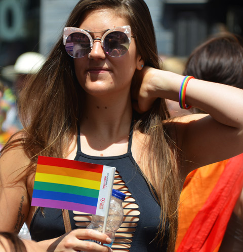 long haired woman holding rainbow flag, wearing sunglasses