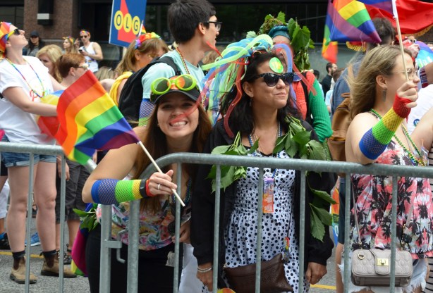 woemn smiling for the camera, dressed up in colourful clothes and holding rainbow flags. 