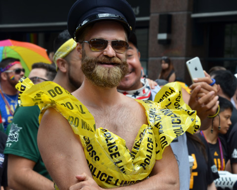 man with bushy beard, a black cap and a top made out of yellow police caution tape 