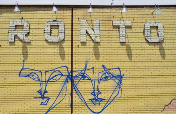 yellow brick wall with two large blue anser faces on it, as well as part of the word Toronto in yellow bricks 