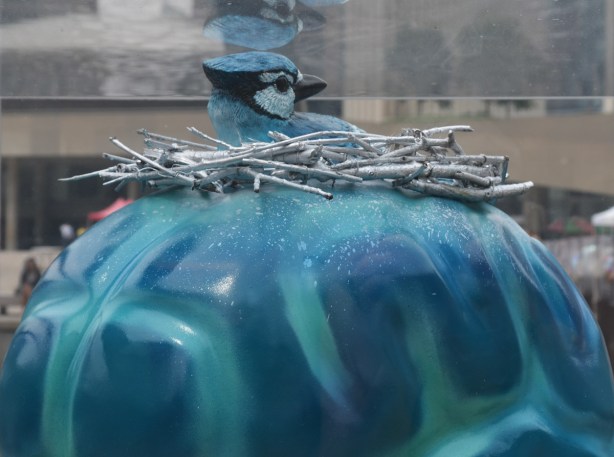 close up of part oa brain sculpture, the brain is painted blue and teal and there is a blue jay sitting on a nest on top of the egg (the bird is part of the sculpture)