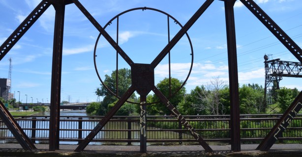 metal work of the side of a bridge frames the view of a river and trees and city buildings, Don River, abandoned bridge