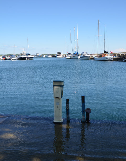 an electrical plug in station stands in the water by a flooded dock at Brigantine Cove, Ontario Place, with sailboats in the background. 