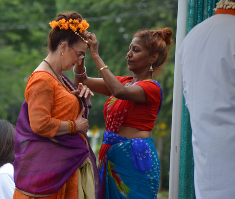 one woman adjusts the floral headband on another woman, both are dressed in traditional South Asian clothing