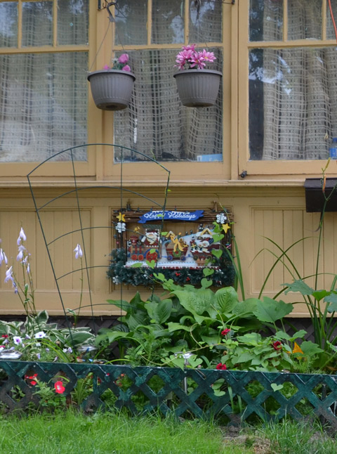 a happy holiday Christmas decoration on the wall at the front of a house, summer flowers growing in front of it. 