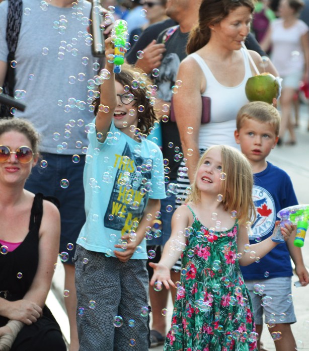 kids playing with plastic bubble shooters in a crowd on the street. 