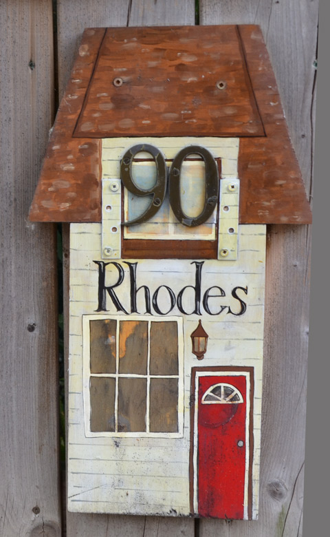 wooden plaque ornament on a wood fence, shape of a house with large window and little red door 