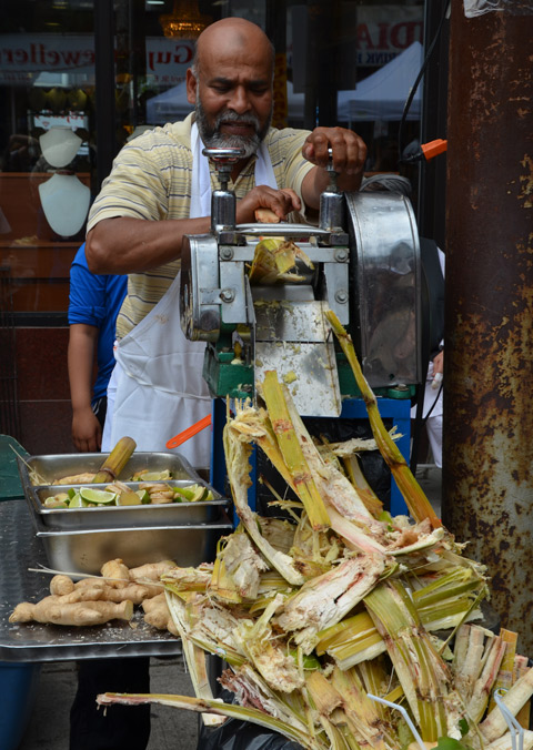 a man shreds sugar cane in a machine to extract the sugar cane juice which he is then selling, outside, street festival, Little India