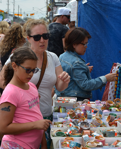 mother and daughter look at bangles, jewellery, for sale outside, at street festival. Both are wearing sunglasses