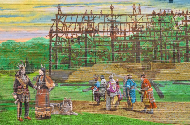 part of a larger mural showing the story of Port Union - two brick buildings, houses, a group of women sitting outside with baskets on the ground, a vintage car 
