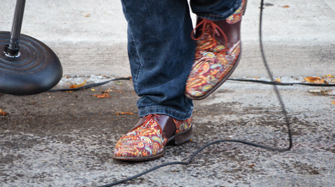 shoes of a man who is moving as he sings, street and sidewalk in the photo 