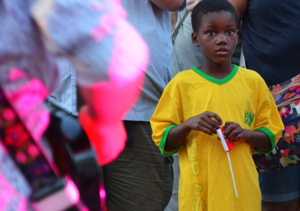 a young boy in a large yellow T-shirt is watching musicians outdoors. 