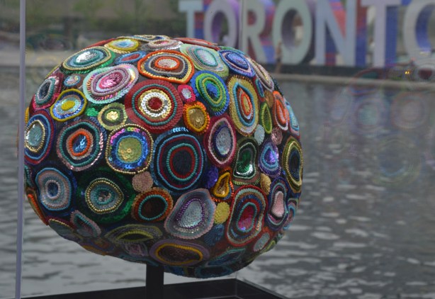 a brain sculpture on display in front of the 3D toronto sign, decorated with colourful circles of sequins
