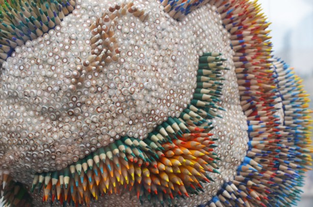 a sculpture of a brain decorated with hundreds of coloured pencils, some are point up and some are blunt end up, the colours of the pencils make shapes and lines on the brain 
