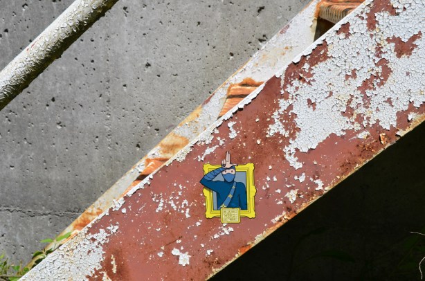 a urban ninja squadron sticker on the side of a metal staircase that was painted brown but the paint is peeling off 