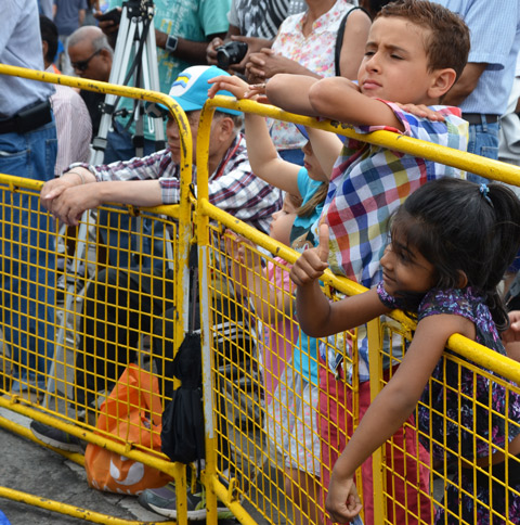 young kids lean over a yellow barricade as they watch a performance a girl is giving a thumbs up sign 