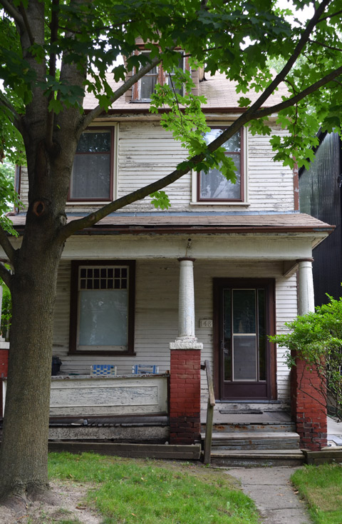 two storey wood frame house with a large porch across the front, pillars by the front steps 
