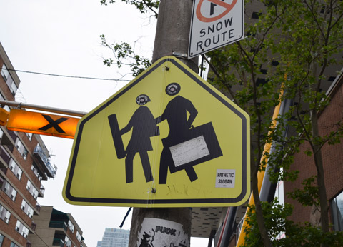 yellow pedestrian crossing sign that has been altered to look like 2 art students, one with a cardboard tube and the other with a portfolio case