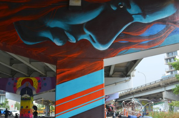 a large blue face mural, horizontal, looking down at the park below 