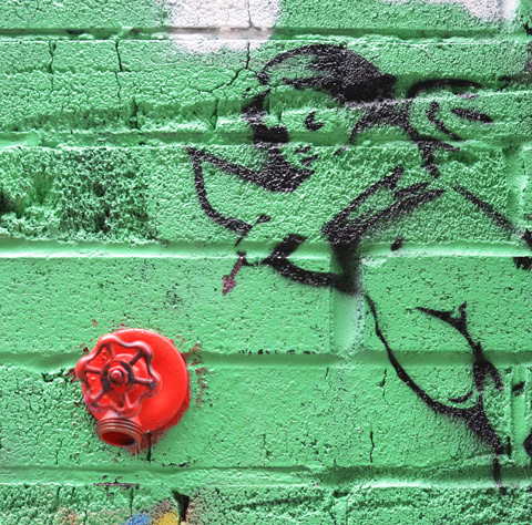green background to a piece of graffiti that is black line drawing of cupid shooting an arrow. The target is a real tap in the wall that has been painted bright red