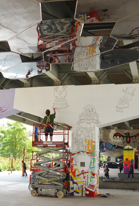 a man is painting a mural on a concrete bent at Underpass park, up on a lift, he is reflected in the mirrors on the ceiling of the park, Al Runt 