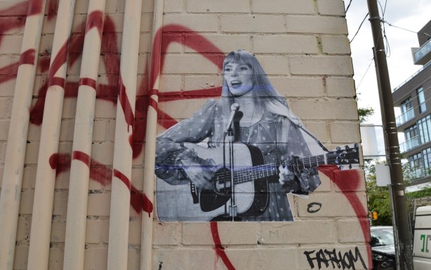 a black and white pasteup of Joni Mitchell playing her guitar and singing 
