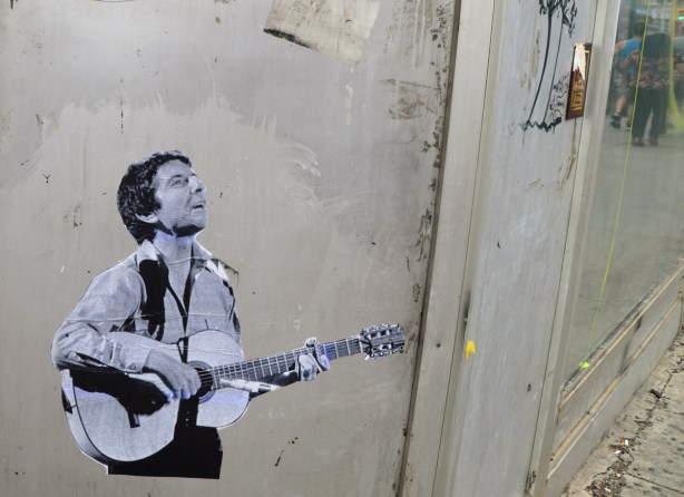 a black and white pasteup of an image of a male guitar player, young man, on a grey wall 