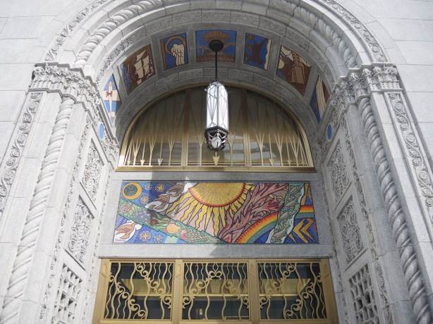 entrance to 100 Adelaide West, a stone building, with brass decorated doors and mosaic pictures decorating it. 