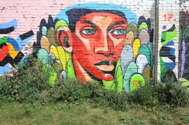 orange face, blue eyes, short black hair, mural on a wall at Sonya Parkette in Kensington