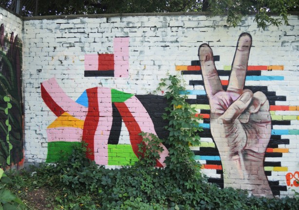 a mural with two parts, on the left is an abstract design with rectangles and a few curves. on the right is a realistic hand giving the peace sign