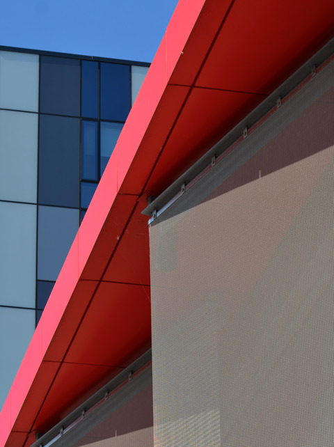 abstract composed of a red roof, a grey textured wall and a building with three tones of blue windows