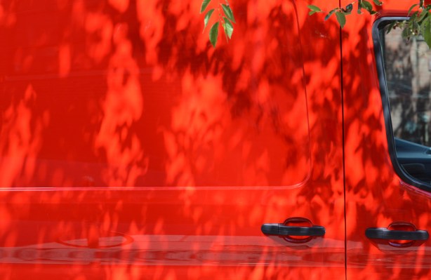 the side of a bright red van, with some leaves and shadows from a small tree