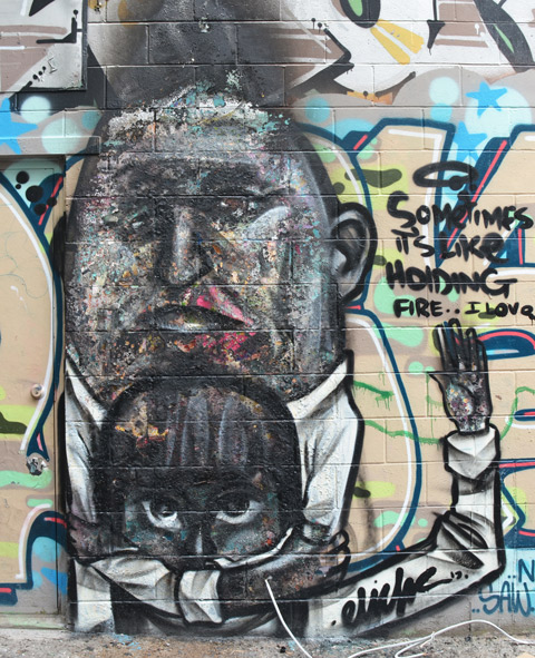 street art by elicser of a man holding (hugging) a child, in blacks and white, with words, sometimes it's like holding fire. 