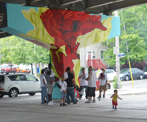a group of people is having a small party in Underpass park, standing around a concrete bent that has recently been painted with a mural by Annie Hamel 