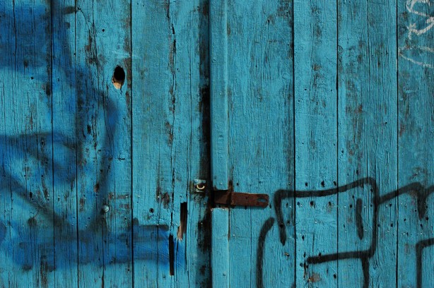 part of an old wood door that is part dark turquoise and part blue, with a rusted latch holding the two doors together and closed 