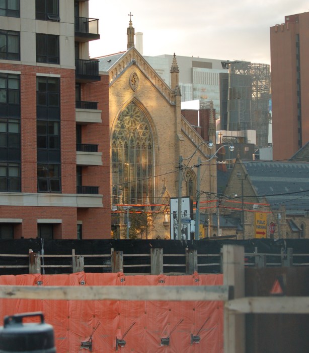 one end of St. Michaels Cathedral with reflected light falling on it, new buildings and construction surround it 