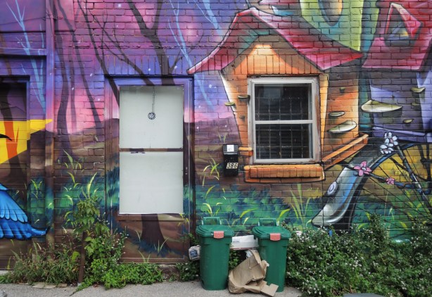 part of a larger mural by Clandestinos (Shalak Attack and Bruno Smoky) on the side of Riders bike store, around the door and window and mailbox of the side entrance of the building,