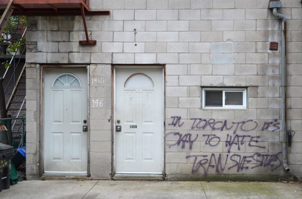 two white doors side by side on a dirty concrete block wall that someone has written the words In Toronto it's okay to hate transvestites
