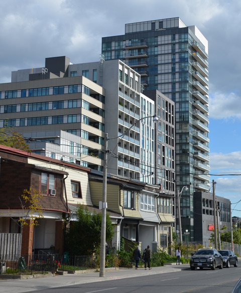In the background, two large high rise buildings, modern, in the foreground, a row of older two storey houses 