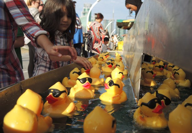 reaching for a yellow rubber ducky with black glasses and bright red lips, ducks are floating in water, a game of luck on the midway at the CNE 