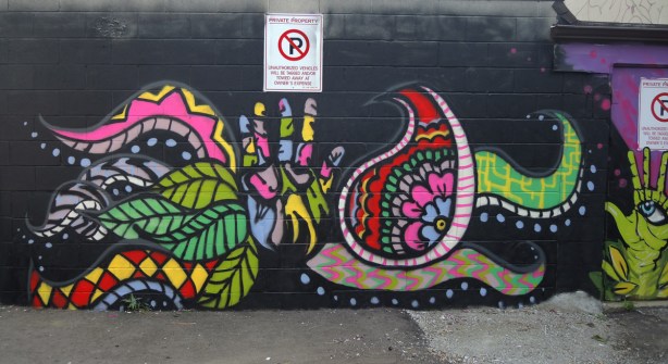 black background mural with stylized floral in bright colours, also a hand in the middle in many colours 