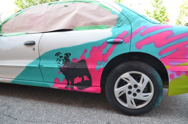 side of a car that has been prepped, for painting partially painted with turquoise section and pink splotches, also a black stenciled dog, called Harley, by the back wheel, 