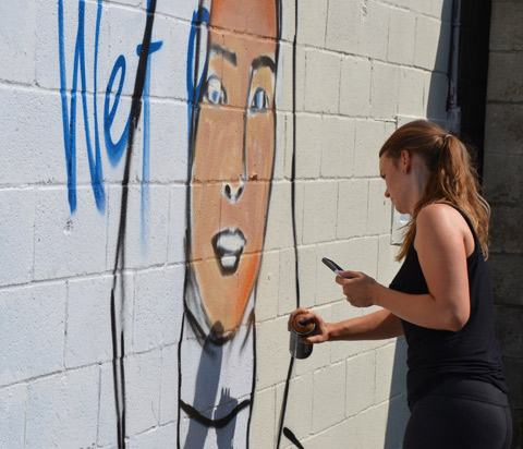 a woman is in the beginning stages of painting a mural portrait of a woman outside
