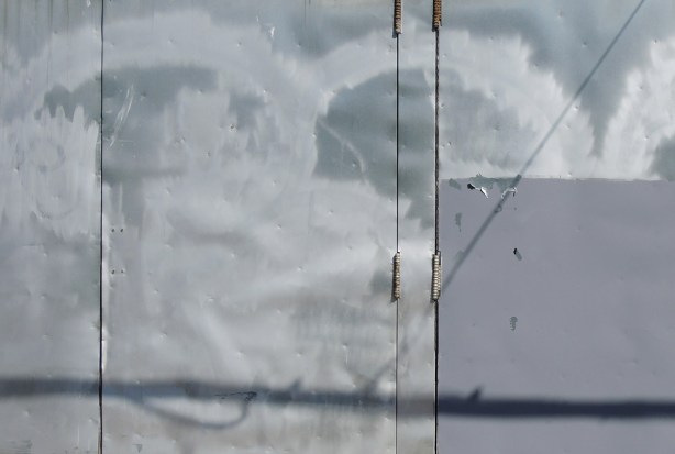 a bashed up grey metal door with splotches of light and shadow